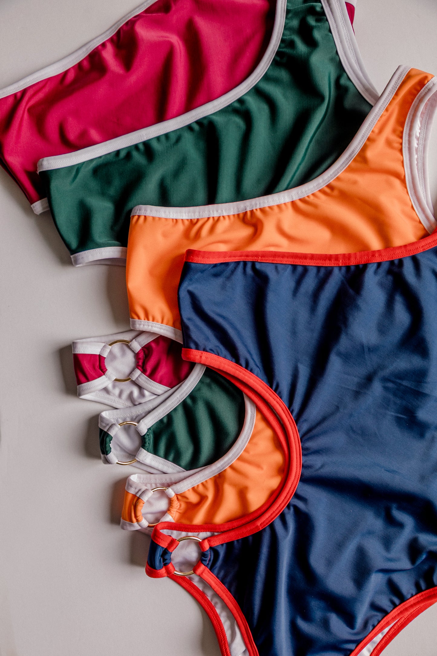 Boomerang one-piece swimsuit, all color variants arranged flatlay – Bikini Uni