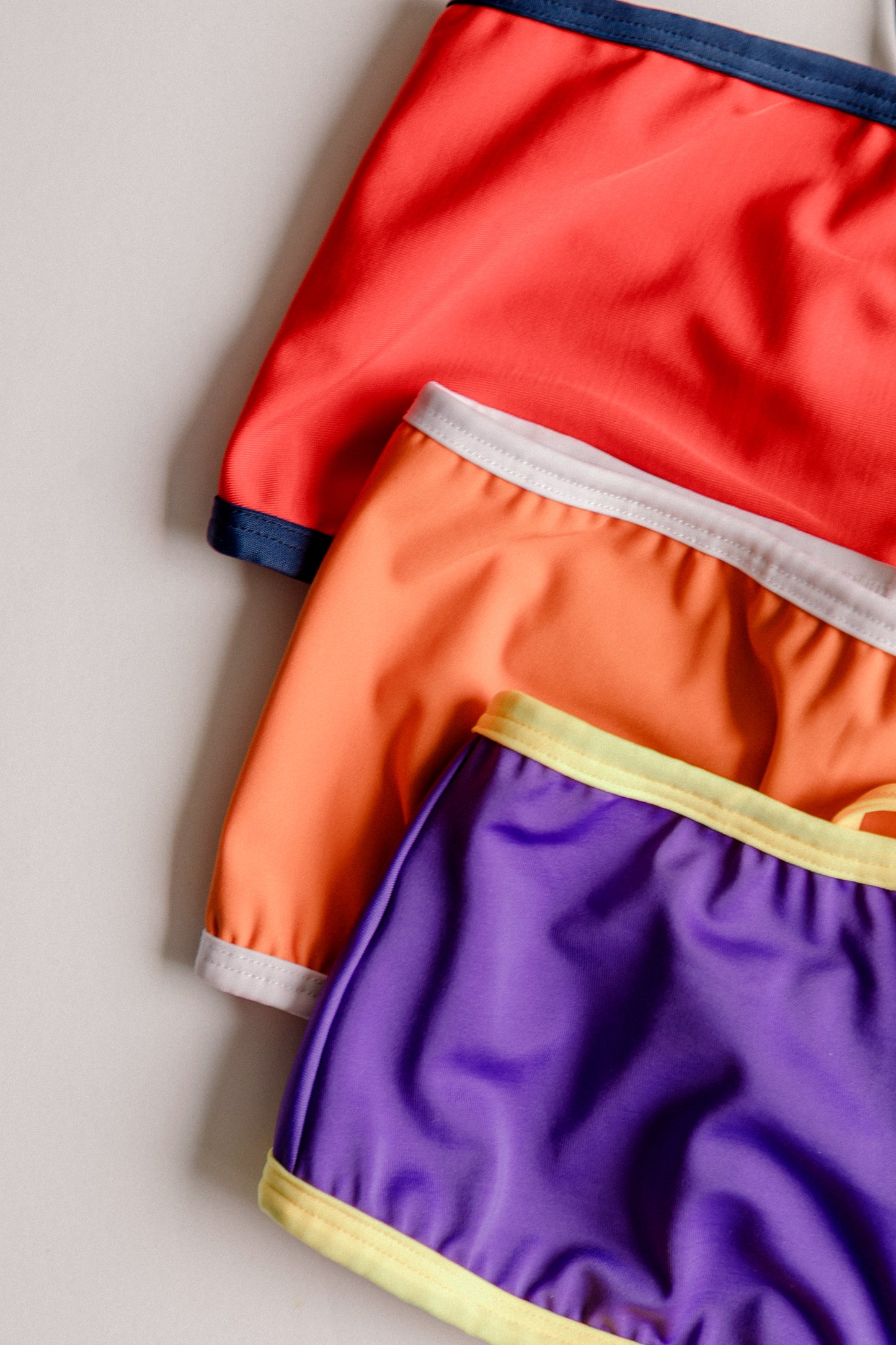 Dos Tierras bikini tops stacked in red orange and purple, close-up – Bikini Uni